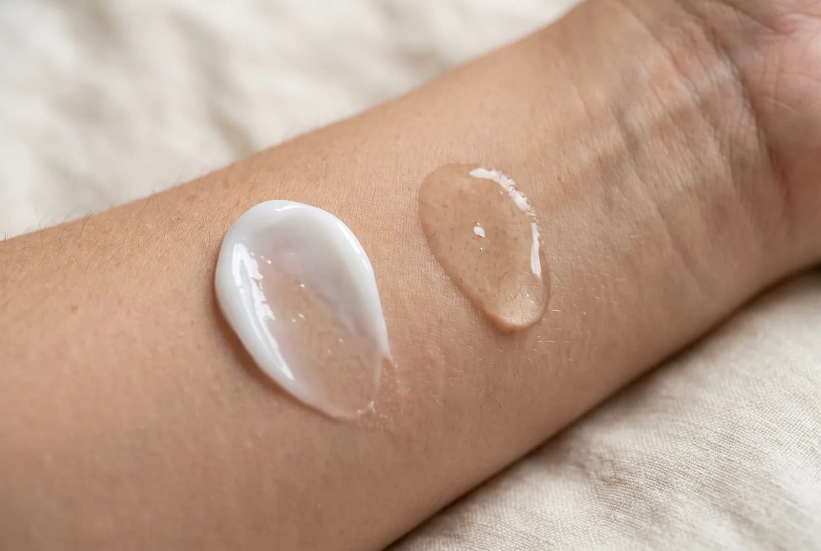 Texturvergleich auf dem Unterarm: weiße Silikoncreme liegt auf, klares Elixier zieht ein